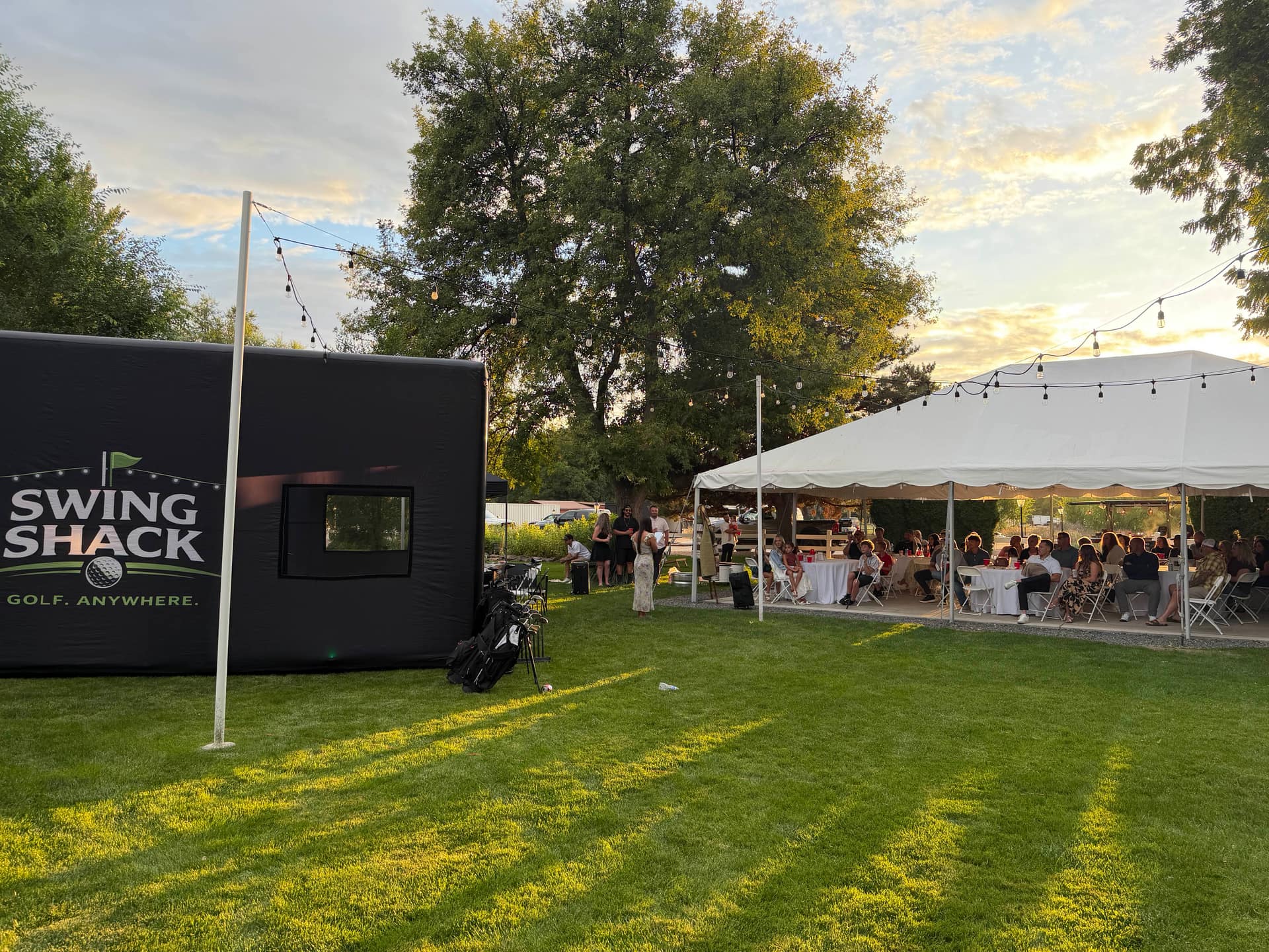 The Swing Shack simulator on a backyard lawn beside a large white tent full of family and friends seated at tables